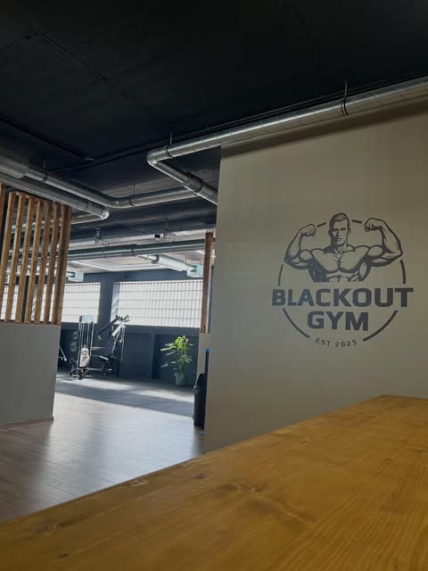 Eingangsbereich mit BLACKOUT GYM Logo an der Wand, dahinter die Trainingsfläche mit Geräten
